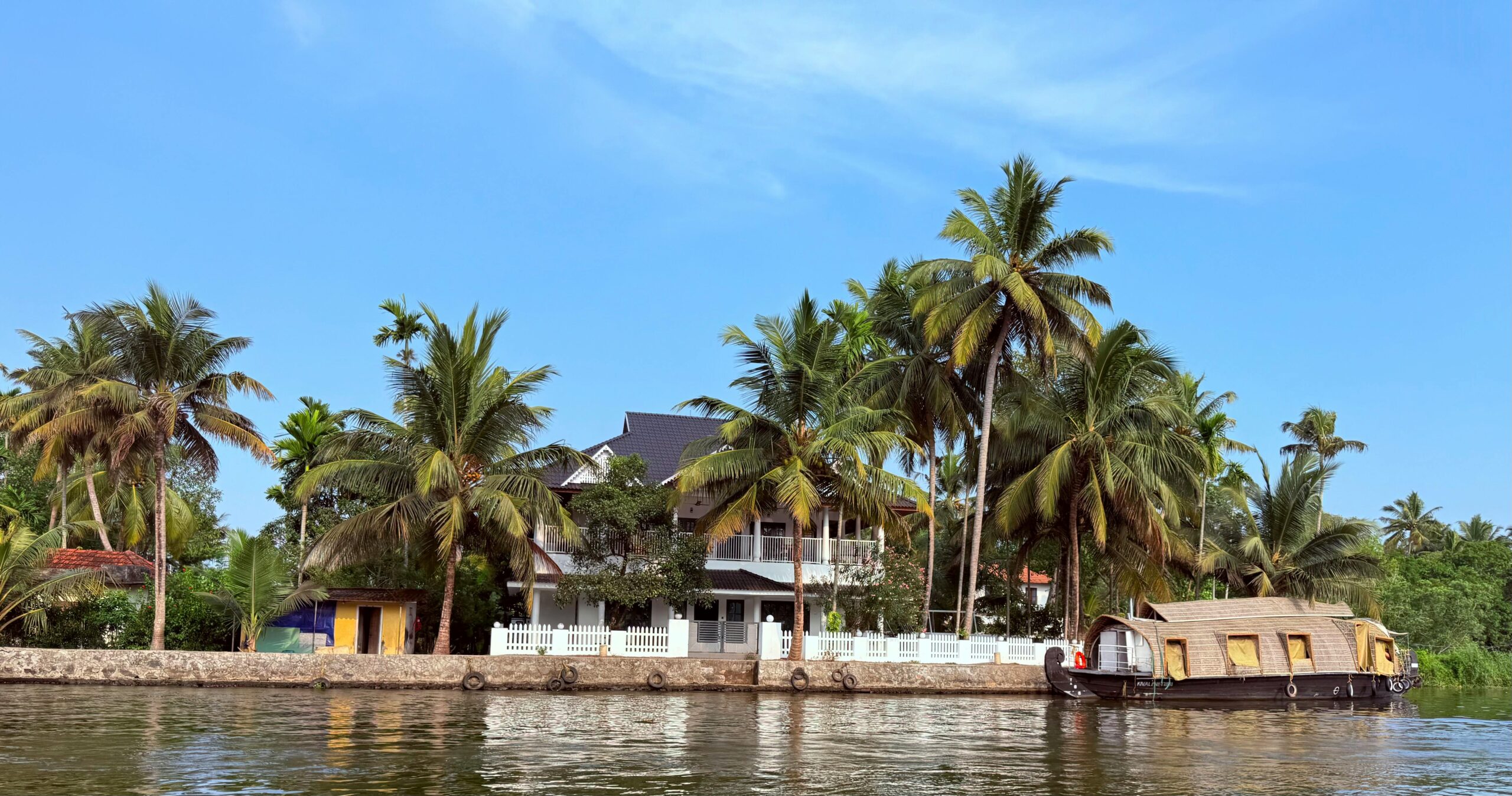 Scenic view of a houseboat by a palm-lined riverbank in Kerala, India.